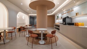 A modern cafe with round tables, orange chairs, a central pillar, and a coffee machine on the counter. - Hostal Bedmates (Barcelona)