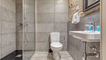 Un baño moderno con cabina de ducha de vidrio, inodoro blanco y lavamanos con espejo.