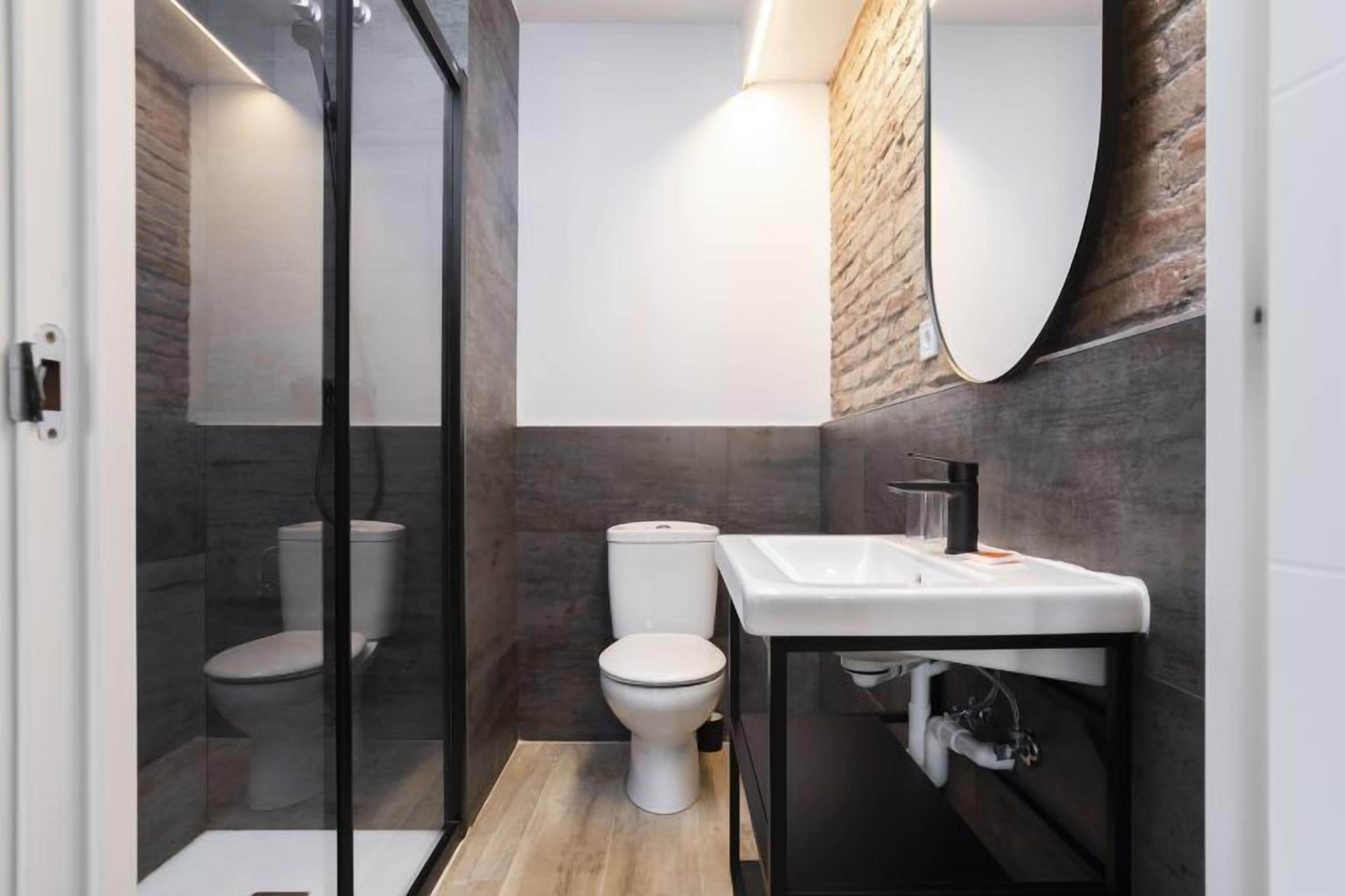 A modern bathroom with a glass shower enclosure, a white toilet, and a black vanity with a mirror.