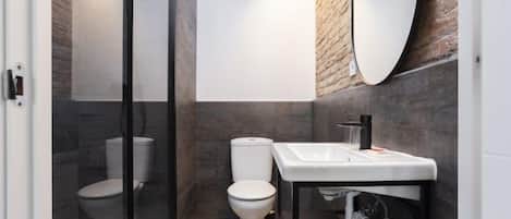 A modern bathroom with a glass shower enclosure, a white toilet, and a black vanity with a mirror.