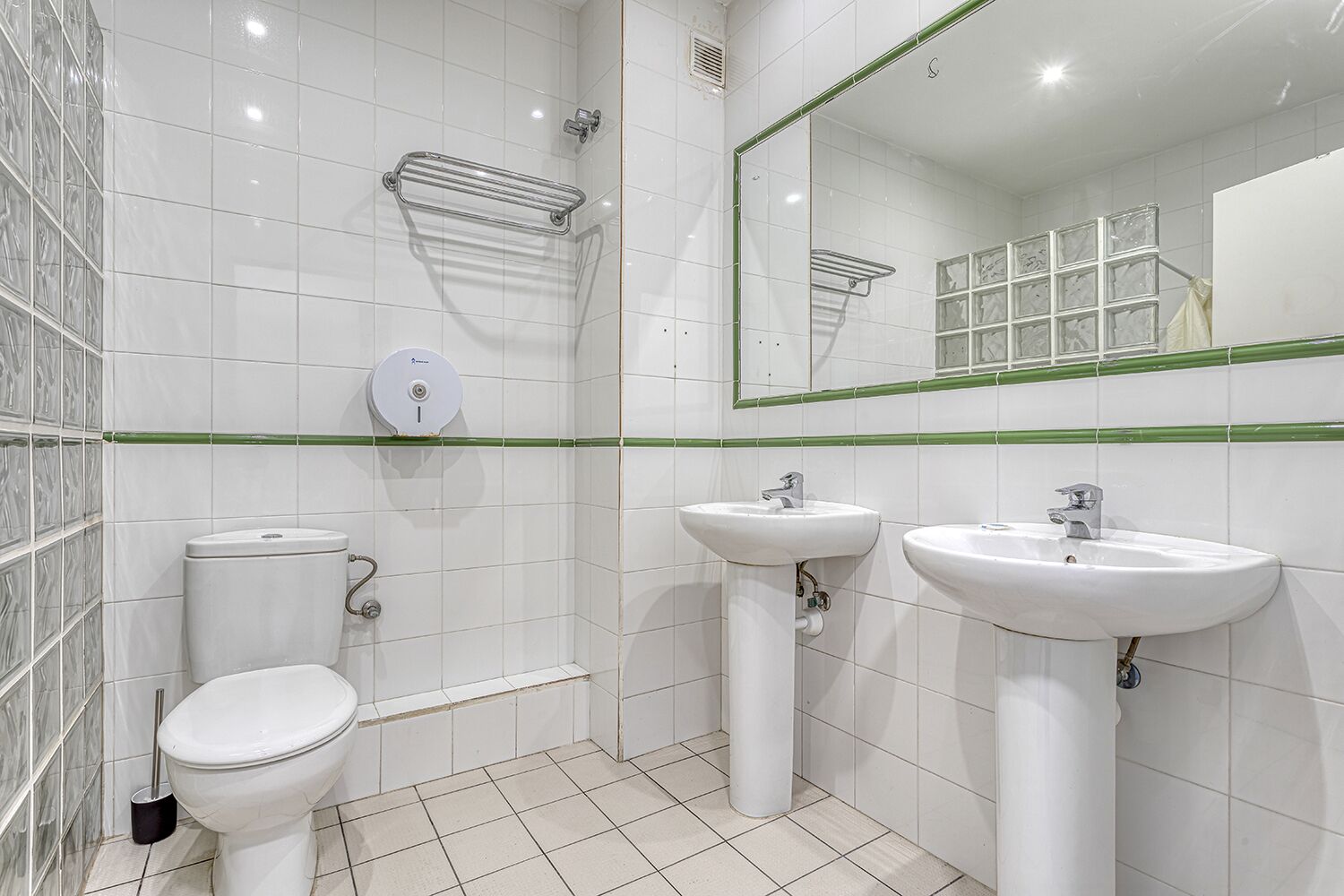 A modern bathroom with a toilet, two sinks, a shower, and a mirror.