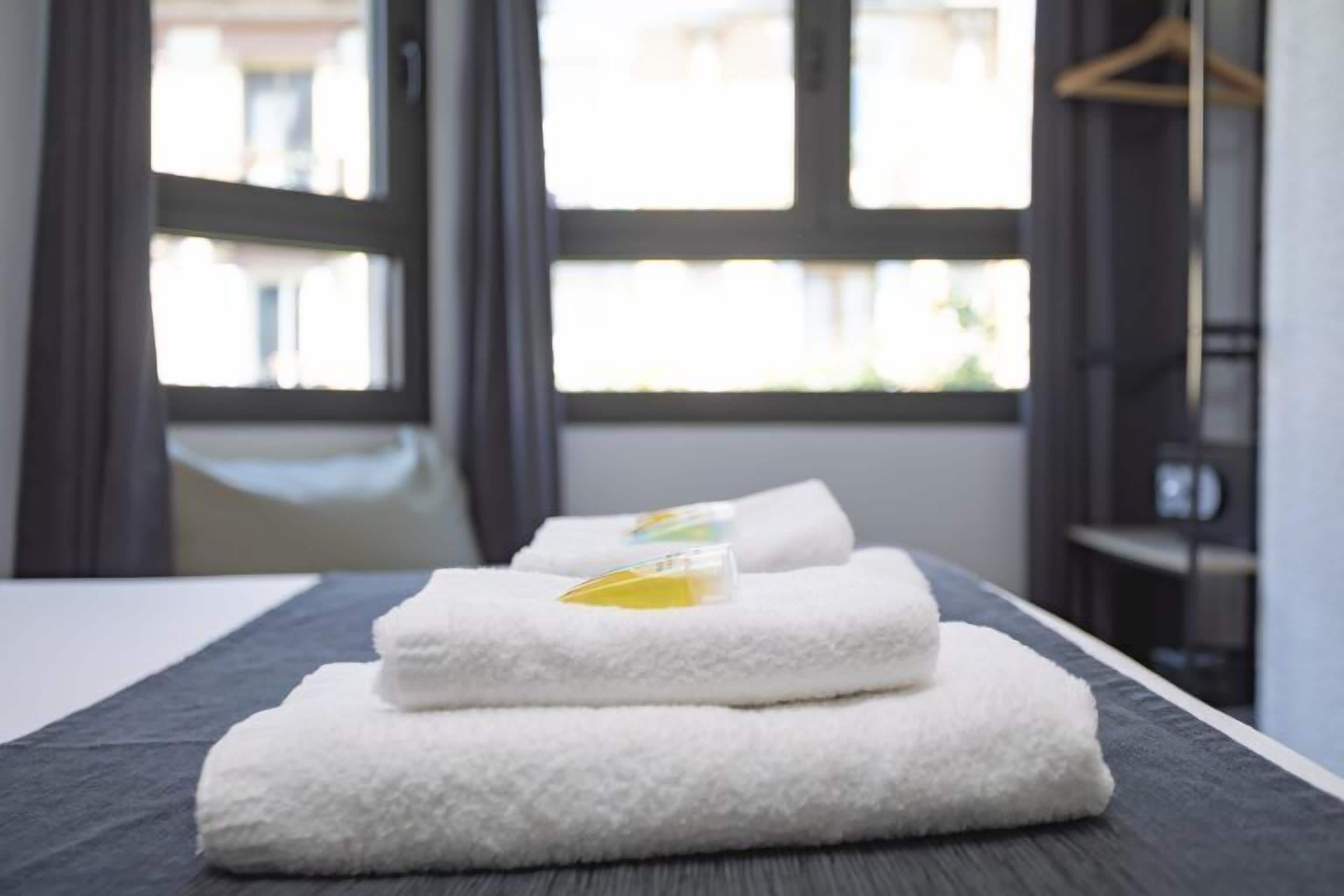 A neatly made bed with folded white towels and a small bottle of lotion on top.