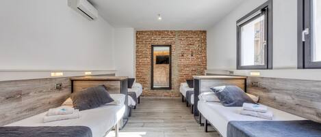 A modern hotel room with two single beds, a brick accent wall, and a large window.