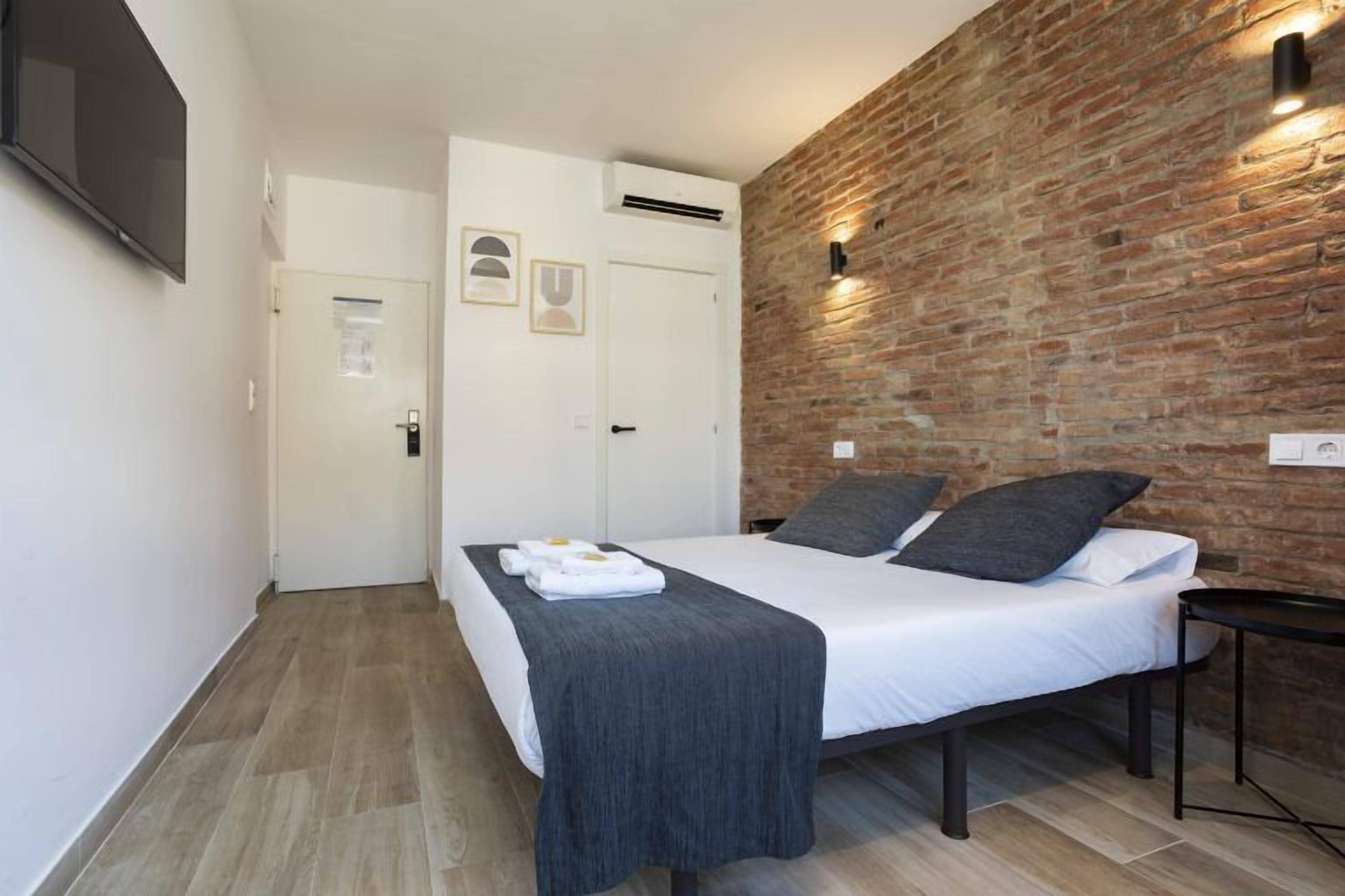 A bedroom with a bed, a brick wall, a flat-screen TV, and a door.
