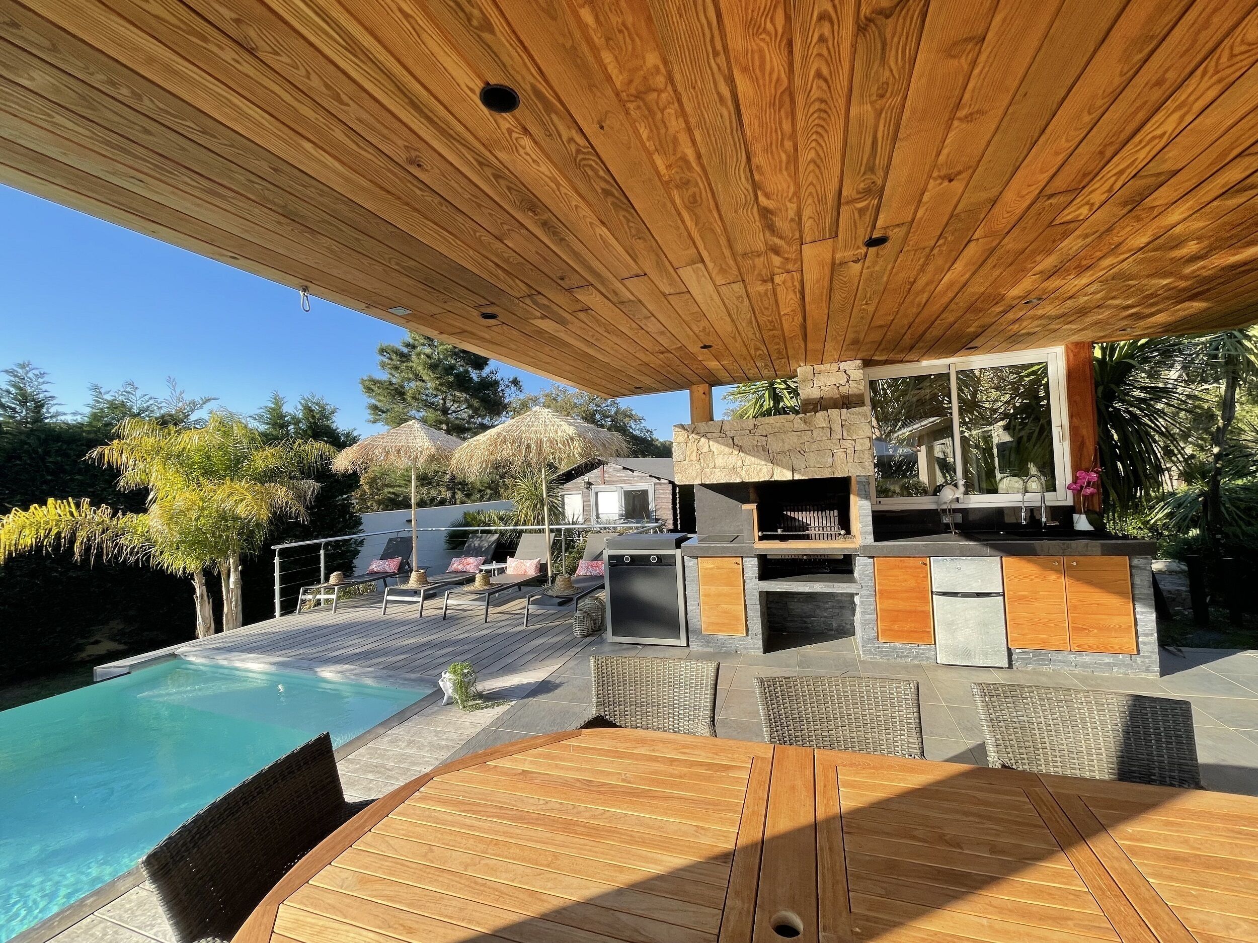 Une terrasse en bois avec une piscine, des chaises longues et une cheminée en pierre.