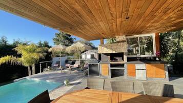 Une terrasse en bois avec une piscine, des chaises longues et une cheminée en pierre.