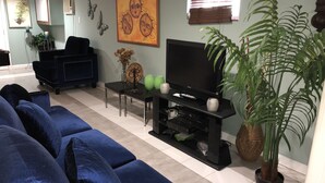 Ein Wohnzimmer mit einer Sofagarnitur, einem Flachbildfernseher, einem Couchtisch, Dekoelementen und einer großen Pflanze.