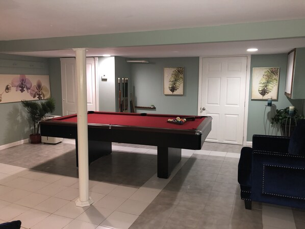 A pool table in a room with teal walls, a white door, and a blue chair.