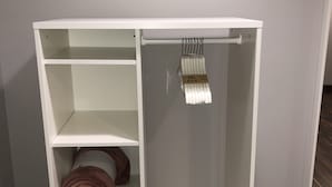Ein weißes Regalsystem mit mehreren Fächern, darunter eine Kleiderstange.