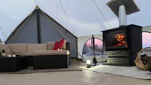 Een knus ingerichte tent met een bank, een open haard en uitzicht op de natuur.