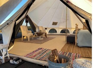 A tent interior with seating, a table, and a small fireplace. - Hruby Doobie Doo Ranch GlampTent (Crown Point)