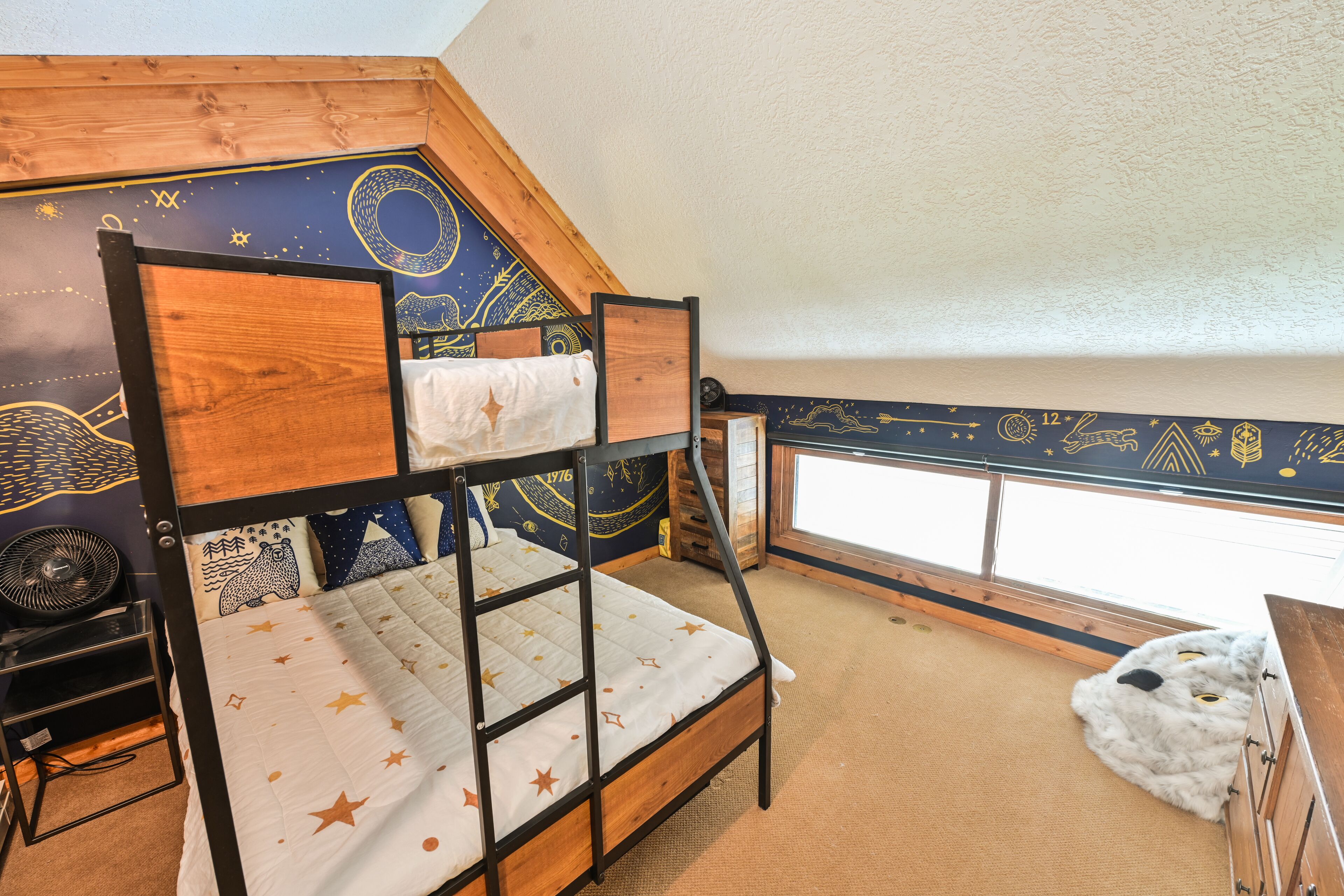A bunk bed with a star-patterned mattress, a wooden headboard, and a ceiling mural.