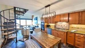 A modern kitchen with wooden cabinets, a central island, and a spiral staircase. - Mountain Views, Hot Tub & Walk to Summer Concerts (Crested Butte)