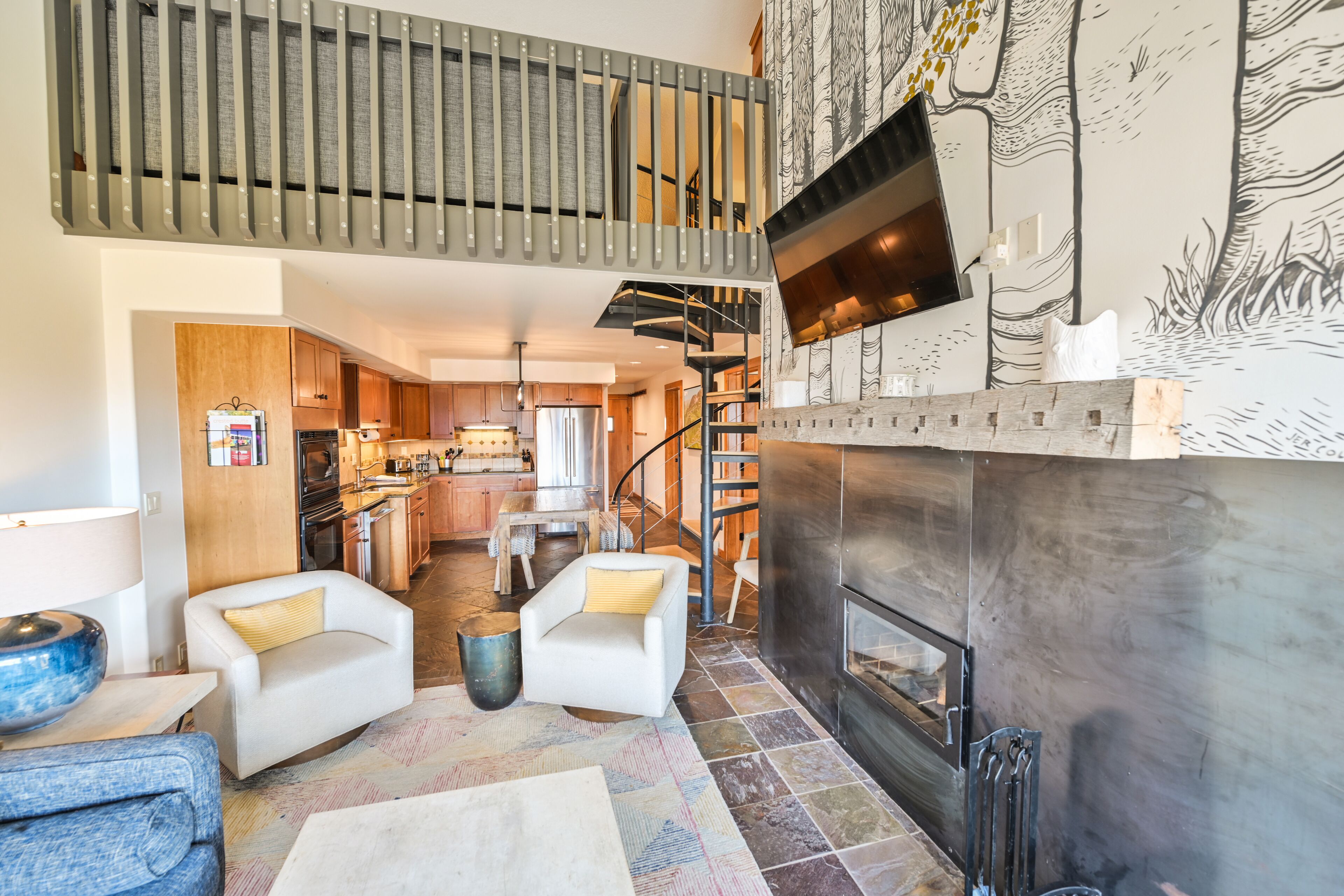 Amplia sala de estar con chimenea, una escalera y una cocina al fondo.