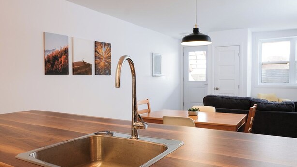 Une cuisine moderne dotée d’un évier en acier inoxydable, d’un plan de travail en bois et d’un coin repas avec une table et des chaises.