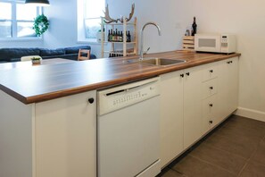 Een keuken met een houten aanrecht, witte kastjes, een vaatwasser en een magnetron.