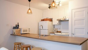 Une cuisine moderne avec un plan de travail en bois, des armoires blanches, un évier en acier inoxydable et un four à micro-ondes. On y trouve trois tabourets en bois et une chaise blanche.