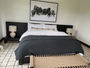 Quarto com uma cama, duas mesas de cabeceira, um quadro na parede e piso estampado.