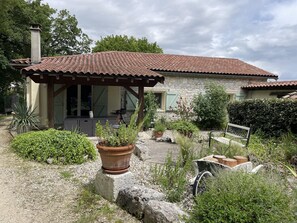 A stone house with a tiled roof, a covered porch, and a garden with potted plants and a bench. - Charming 4* gîte with private pool&jacuzzi 11 bedrooms/10 bathrooms (Touffailles)