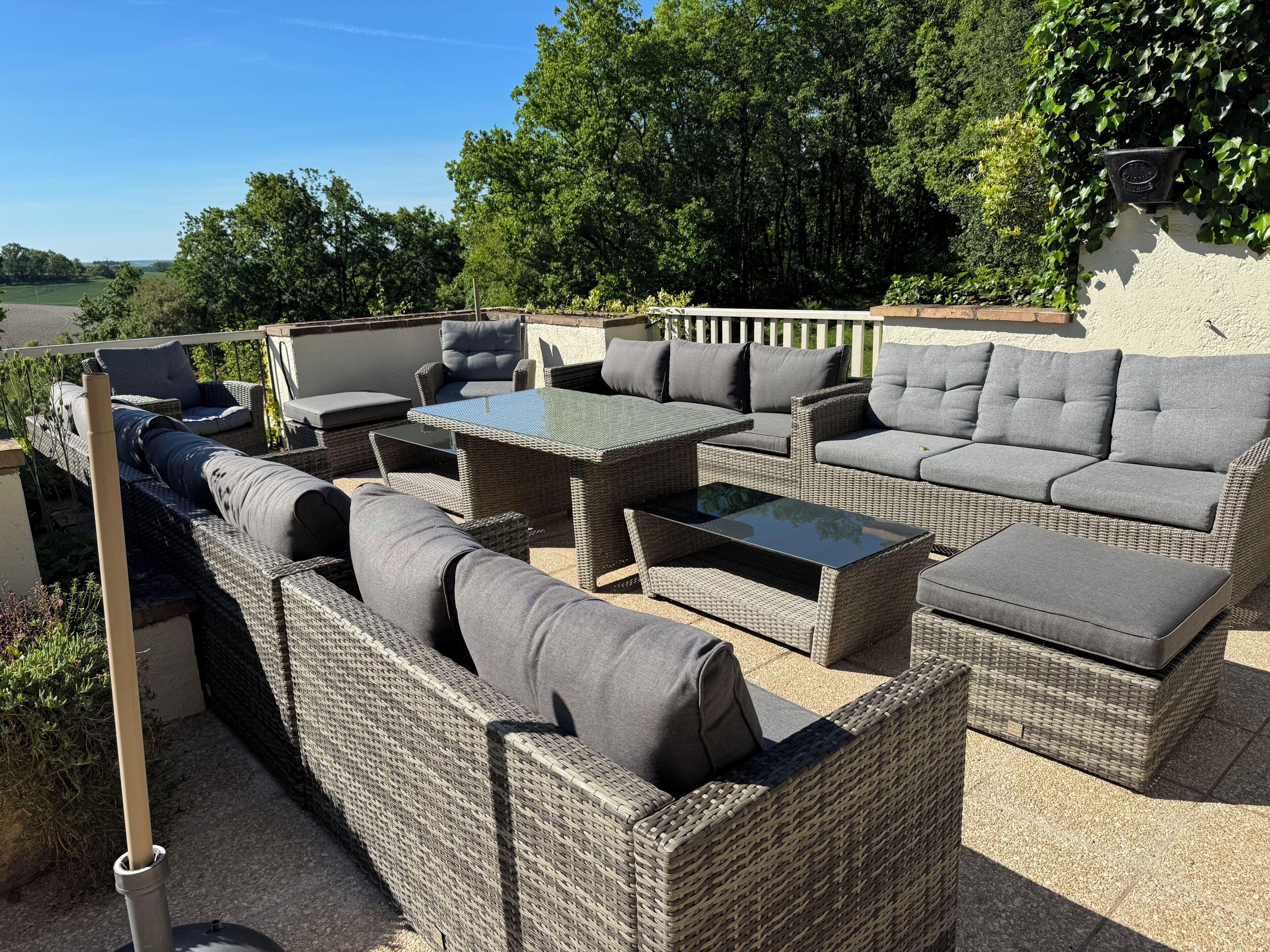 Un patio exterior con mobiliario de mimbre, incluyendo sofás y una mesa, y vistas del paisaje circundante.
