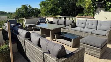 Un patio exterior con mobiliario de mimbre, incluyendo sofás y una mesa, y vistas del paisaje circundante.