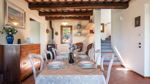 A dining area with a table set for six, wooden chairs, a vase with flowers, and a rustic ceiling.
