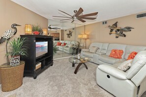 A living room with a flat-screen TV, a ceiling fan, a sofa, and decorative wall art.