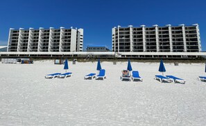 A beachfront hotel with multiple floors, outdoor seating areas with blue umbrellas, and a clear view of the ocean.