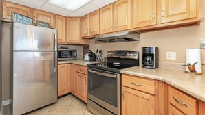 Una cocina con gabinetes de madera, electrodomésticos de acero inoxidable, microondas, cafetera y tostadora.