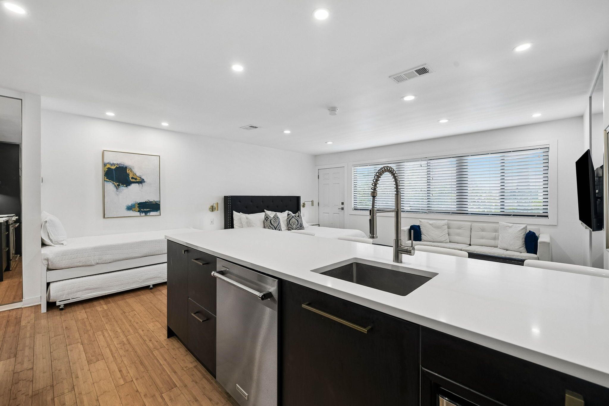 A modern kitchen with a central island, a built-in dishwasher, and a large window with blinds.
