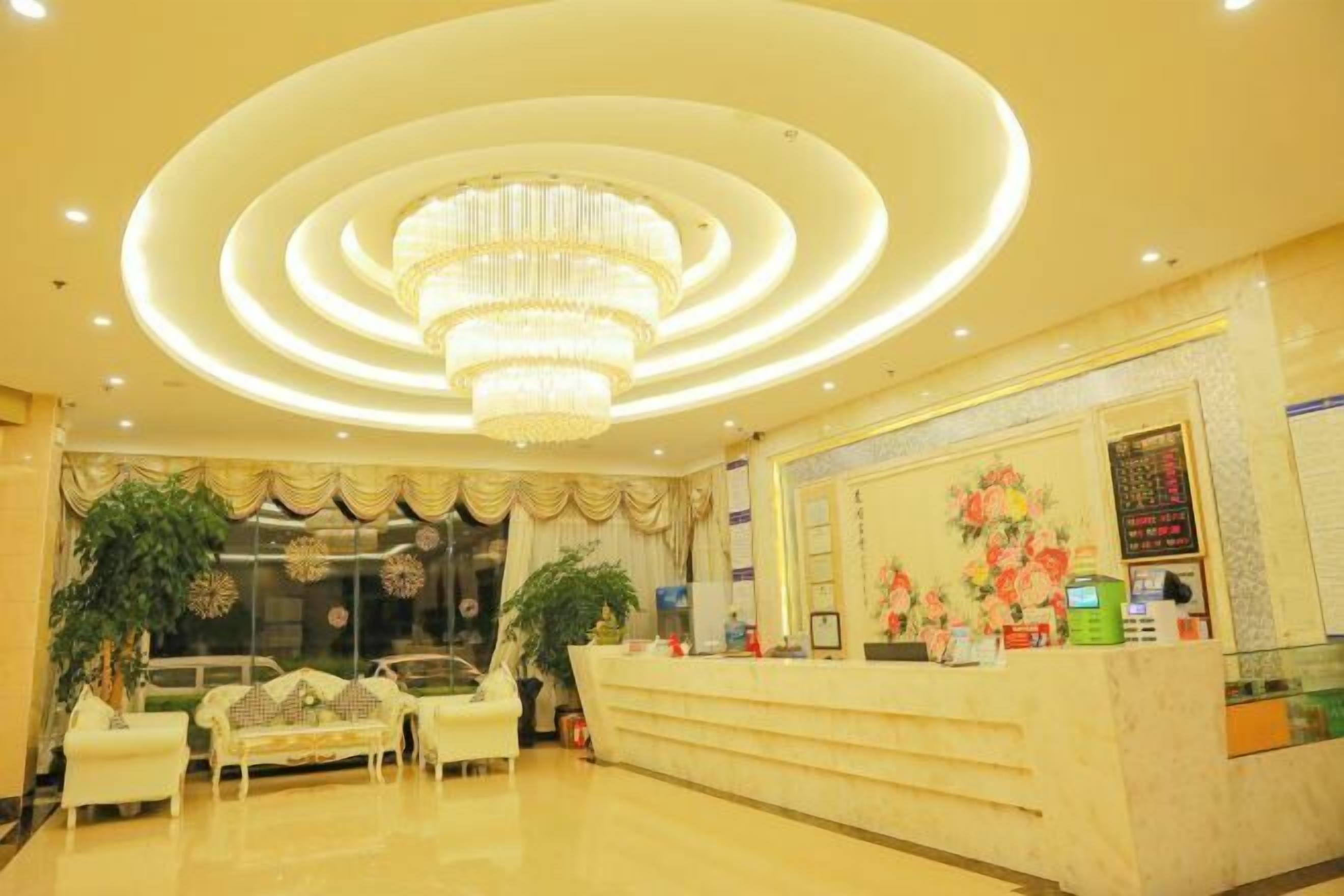 A hotel lobby with a reception desk, seating area, and a chandelier.