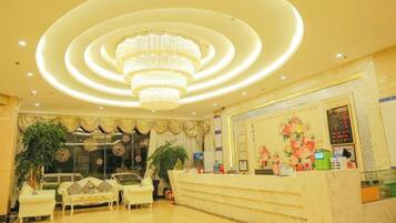 A hotel lobby with a reception desk, seating area, and a chandelier.