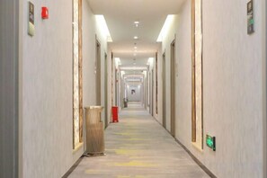Un largo pasillo de hotel, estrecho, con puertas a ambos lados, un basurero y un objeto rojo a lo lejos.