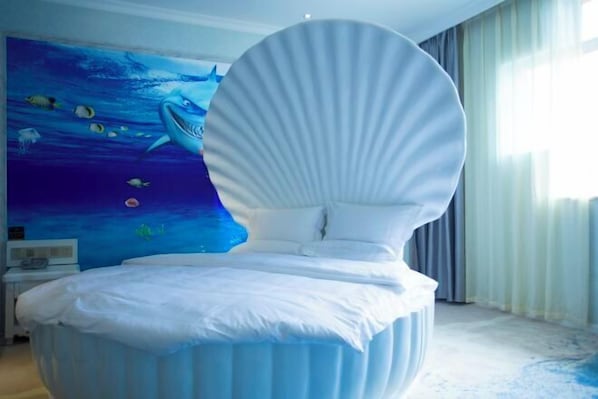 Ein modernes Schlafzimmer mit einem einzigartigen Bettleibdesign, einem Wandgemälde mit Unterwasser-Szene und einem großen Fenster mit Vorhängen.