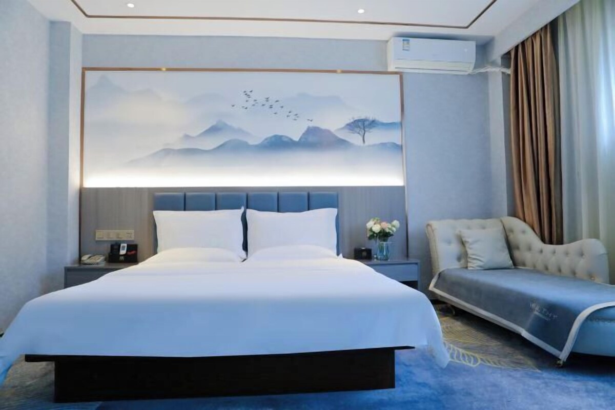 Une chambre d’hôtel moderne avec un grand lit, une table de chevet, une chaise et un climatiseur fixé au mur.