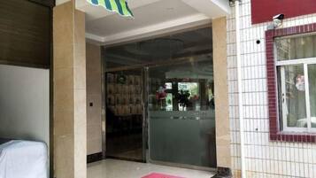 A hotel entrance with a glass door, a tiled floor, and a red mat.
