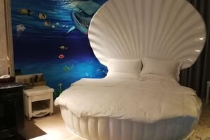Un lit avec une tête de lit à bords festonnés, dans une pièce ornée d’une fresque représentant un paysage sous-marin.