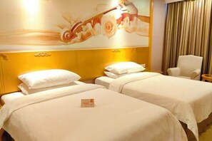 Quarto de hotel com duas camas, cabeceira com desenho floral, uma cadeira branca e uma pequena mesa.