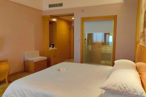 A hotel room with a bed, a bedside table, a chair, a mirror, and a door leading to a bathroom.