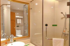 A hotel bathroom with a glass-enclosed shower, a sink with a mirror, and a toilet visible through the glass.