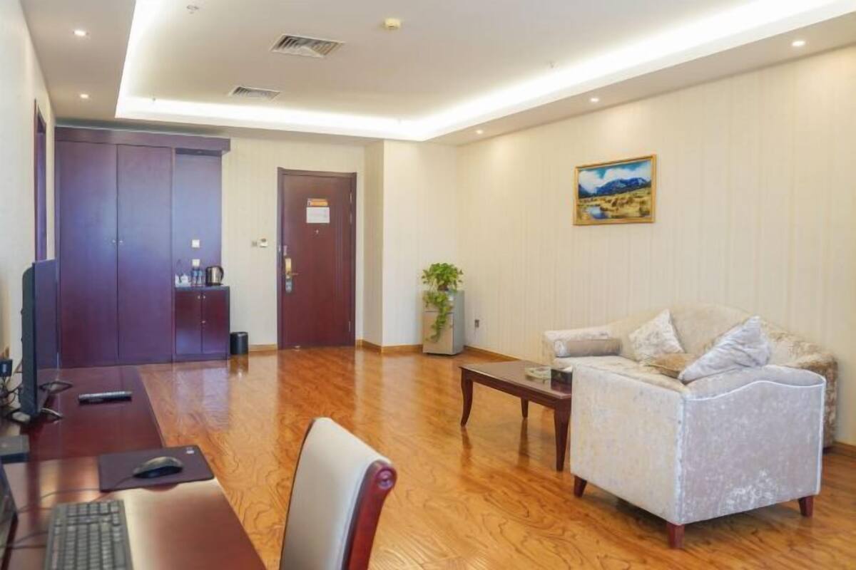 A room with a wooden floor, a sofa, a desk with a computer, a television, and a door.