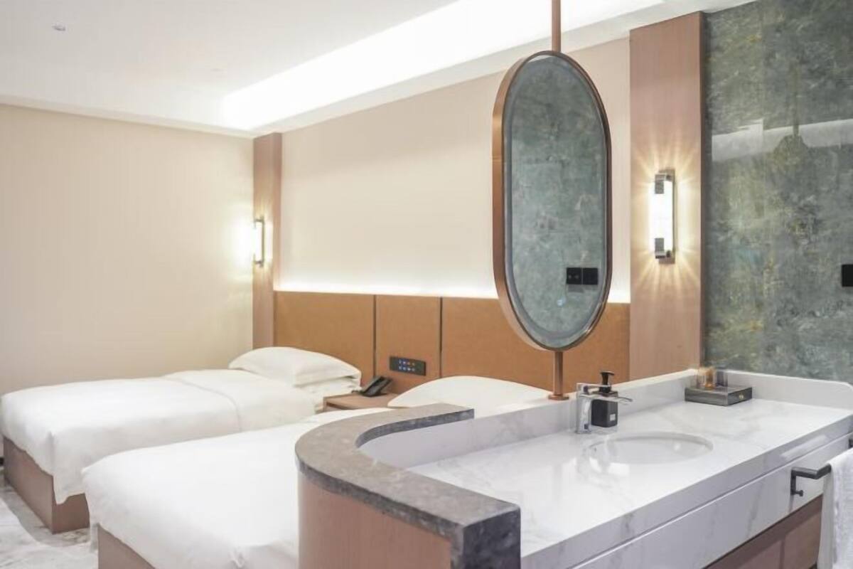 A hotel room with two beds, a large mirror, a marble bathroom vanity, and a wall-mounted light fixture.