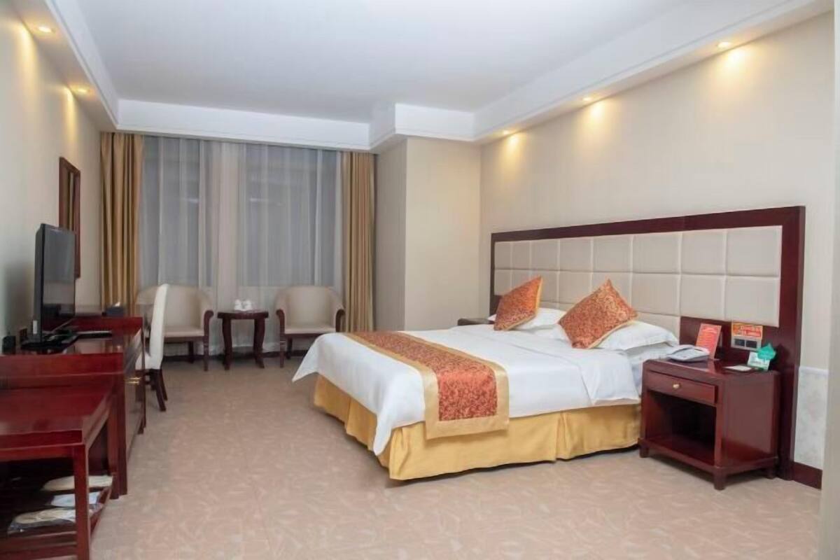 A hotel room with a large bed, a desk, a chair, and a TV.
