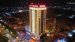 A high-rise hotel with multiple floors, a parking lot, and a brightly lit facade. - Kangtai Hotel (Hanggin Banner)
