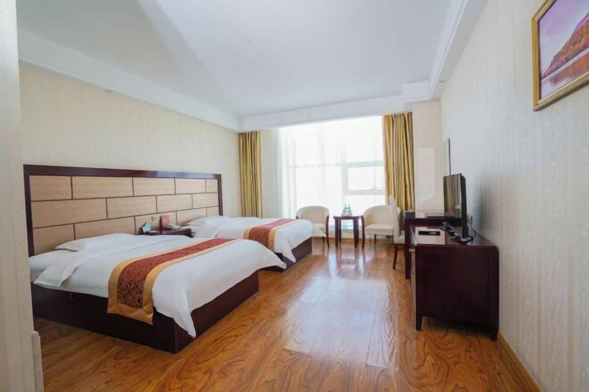 A hotel room with two beds, a desk, a chair, and a television.