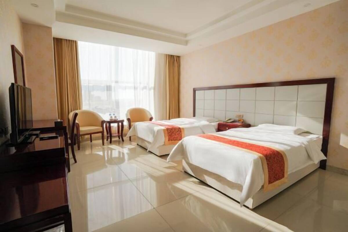 A hotel room with two beds, a desk, a chair, and a television.