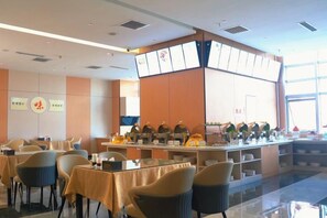 Un restaurante con mesas, sillas, una barra con productos alimenticios y un amplio ventanal.