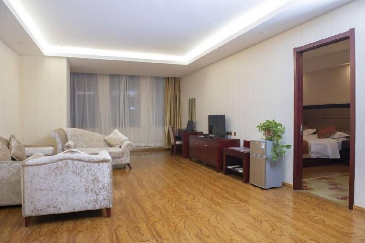 A modern hotel room with a wooden floor, a sofa, a desk, a television, and a bed.