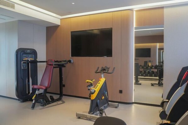 Un gimnasio con equipo de ejercicio que incluye una prensa de banca, una bicicleta estática y una pantalla de televisión.