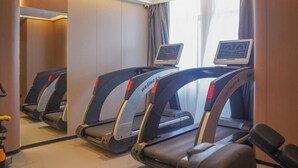 A hotel room with three treadmill exercise machines, a window with curtains, and a small desk with a computer monitor. - Kangtai Hotel (Hanggin Banner)